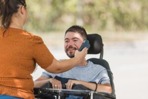 Female,Assistant,Helping,A,Man,With,Disability,Use,A,Smartphone.